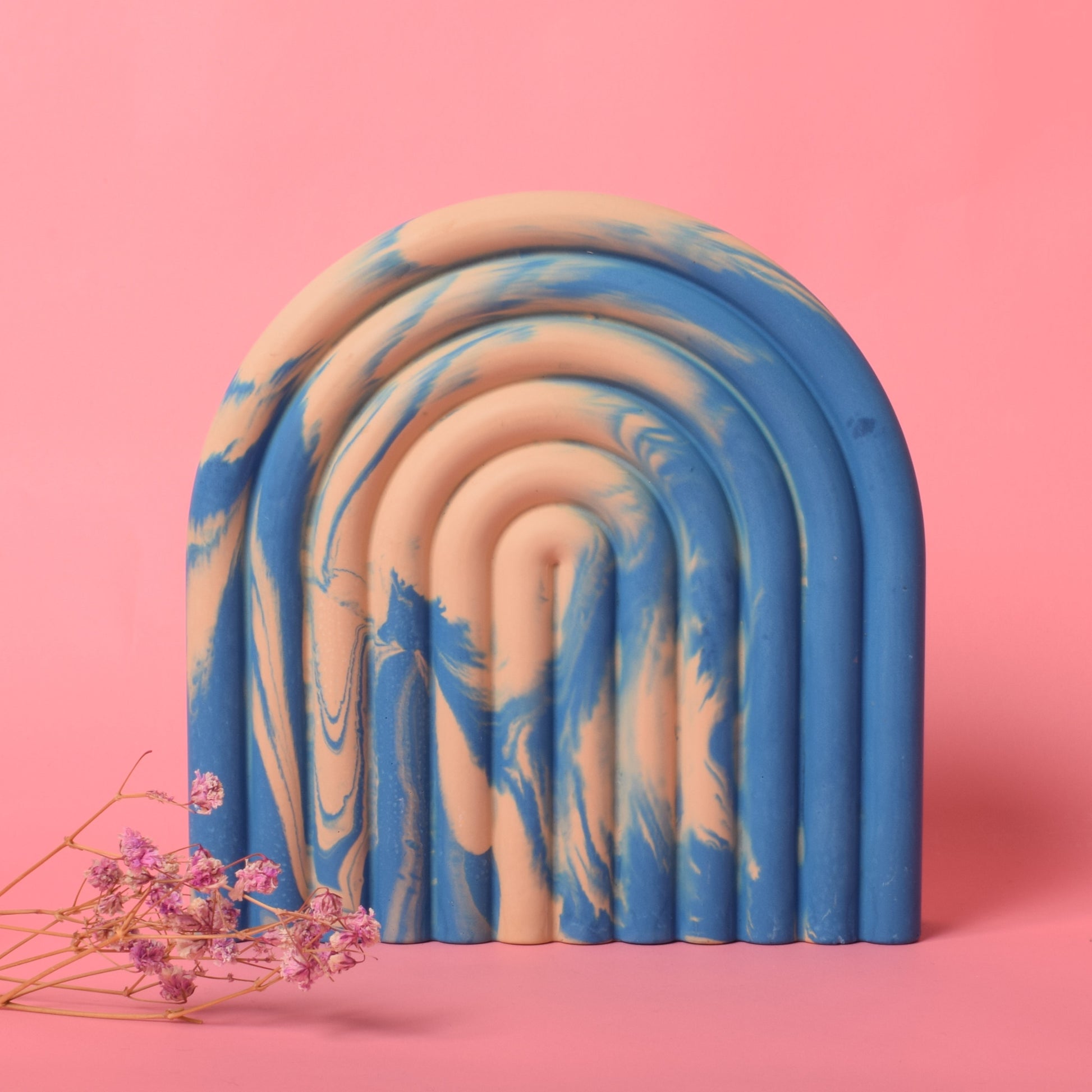 A blue and beige marble effect arched bookend with dried flowers in front of it.