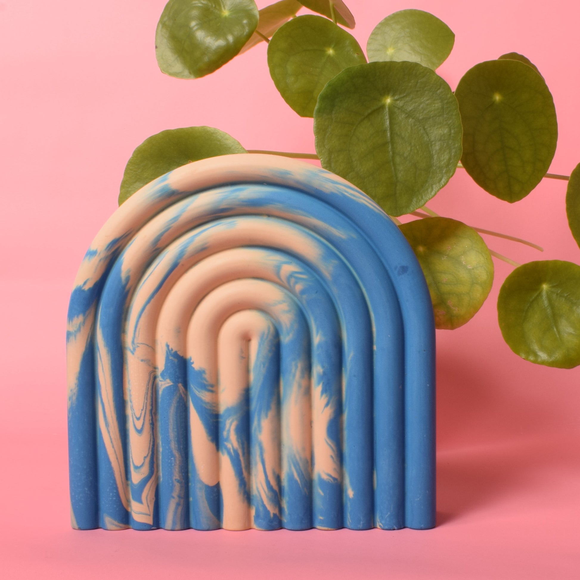 A blue and beige marble effect arched bookend with a plant behind it.