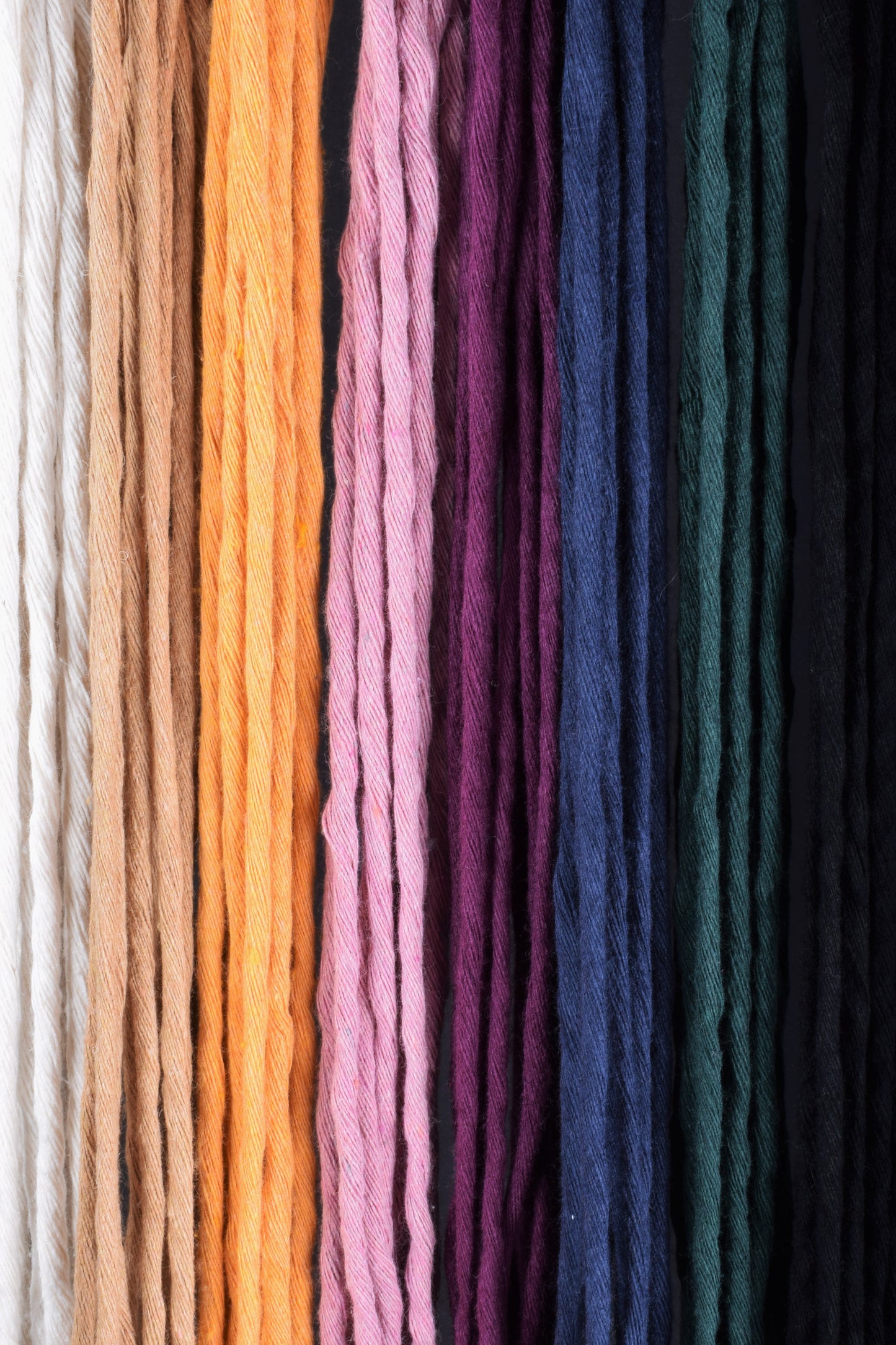 White, beige, yellow, pink, purple, blue, green and black recycled cotton cord lined up.