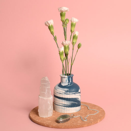 A navy blue and white marble effect ribbed vase holding flowers. It is on a cork mat, next to a selenite tower and a crystal pendant.