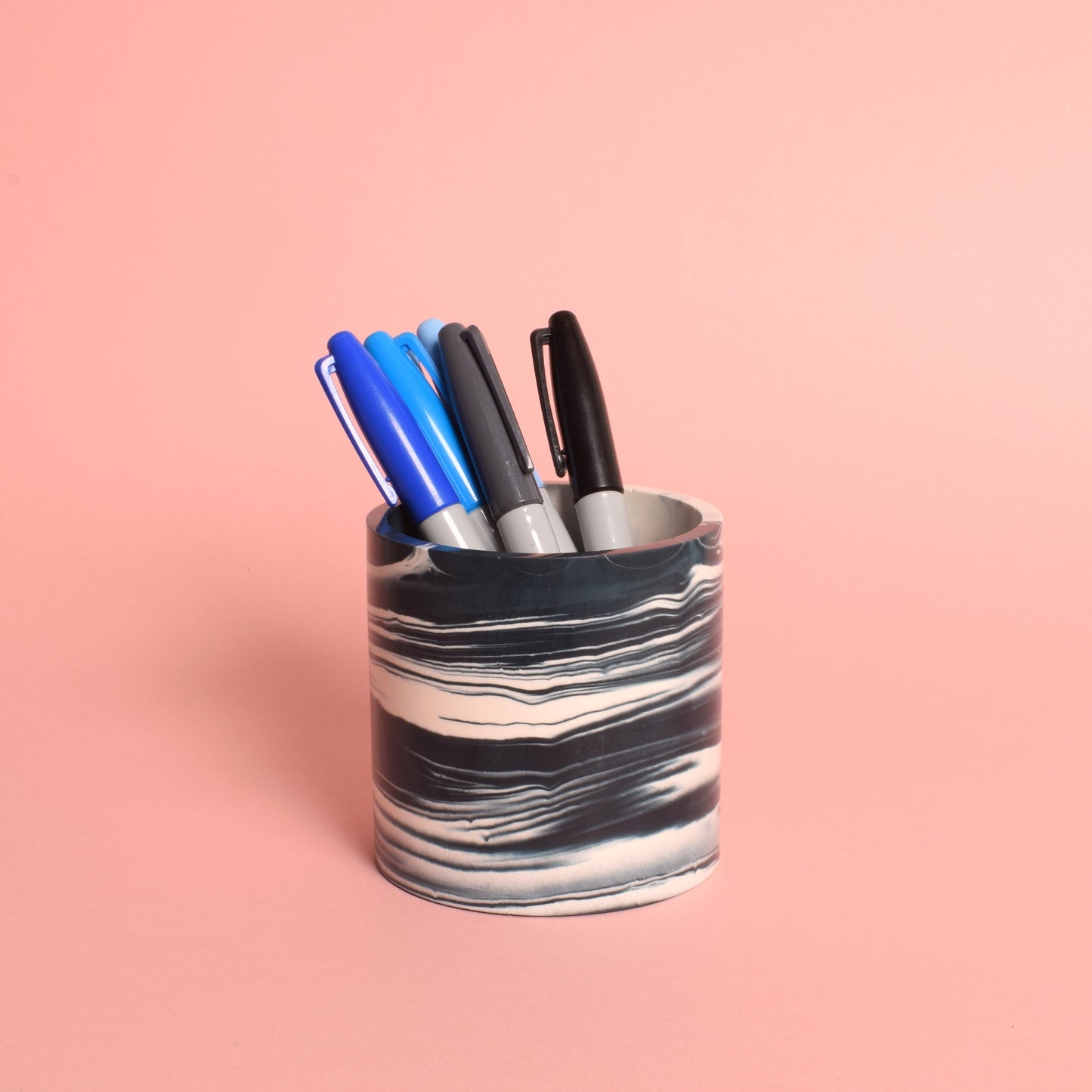 A marble effects navy blue and white multi-use pot holding blue and black sharpie pens.