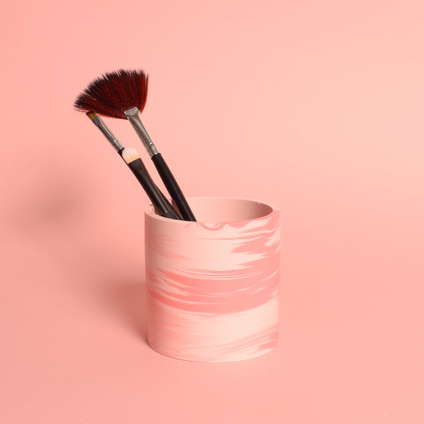 A marble effect pink multiuse pot holding makeup brushes.