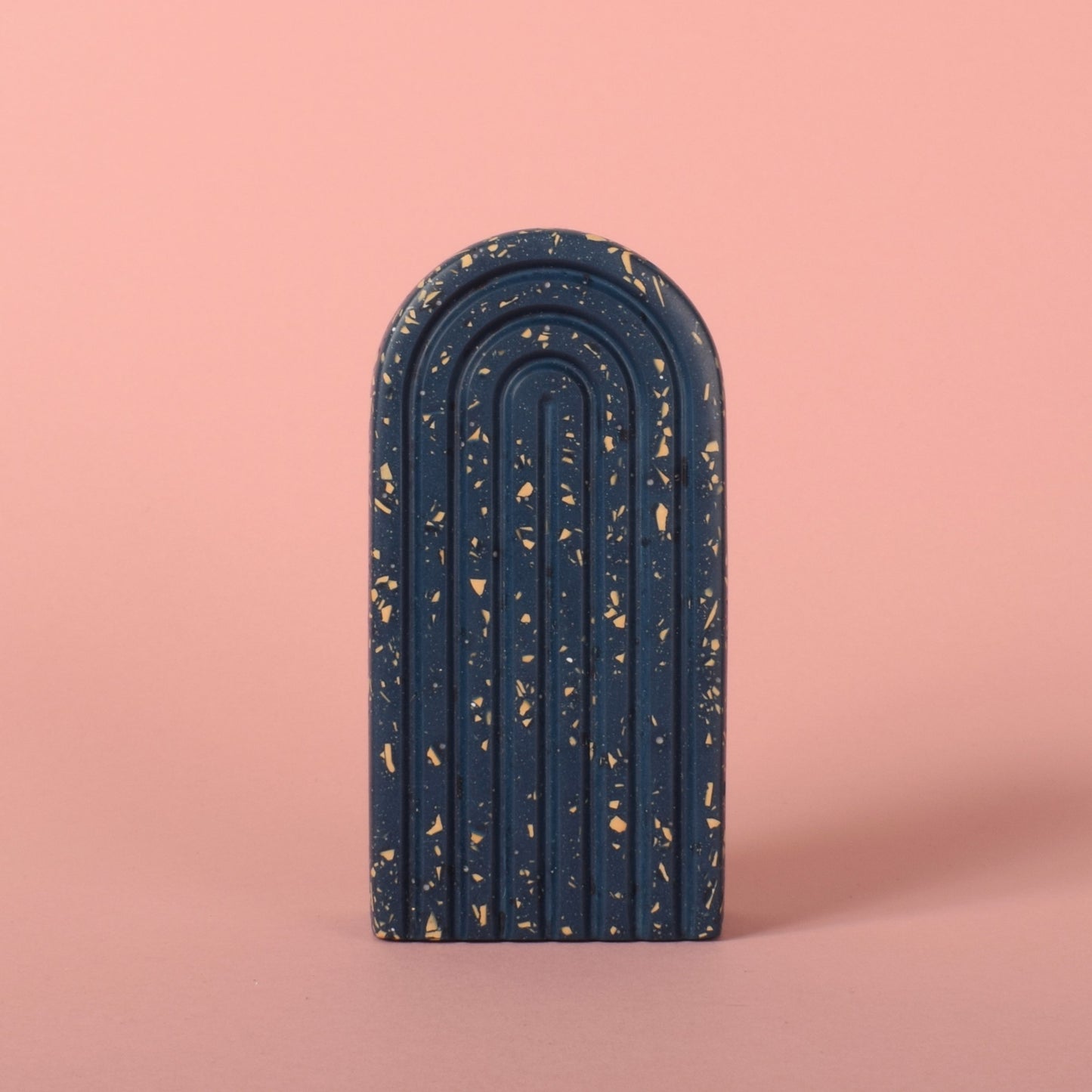 A small navy blue arched bookend with beige terrazzo chips in it.