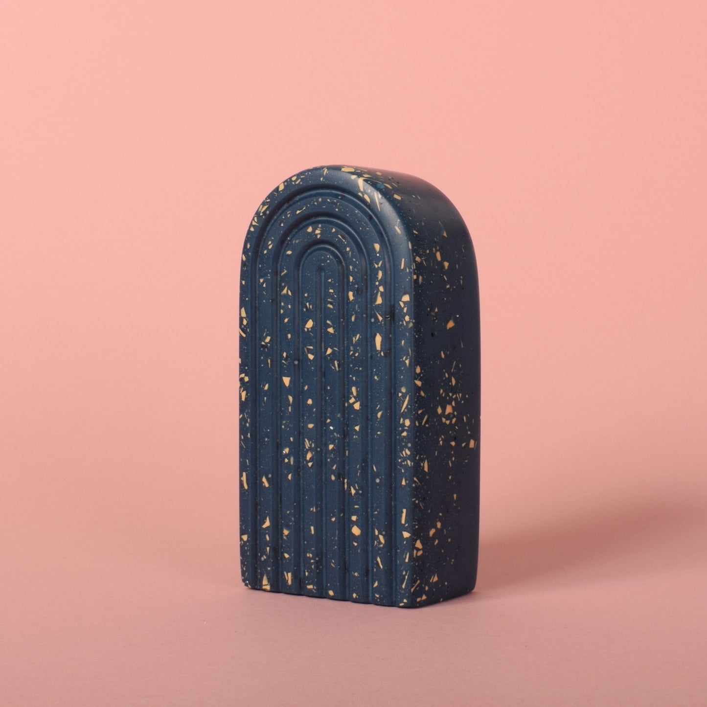 A small navy blue arched bookend with beige terrazzo chips in it.