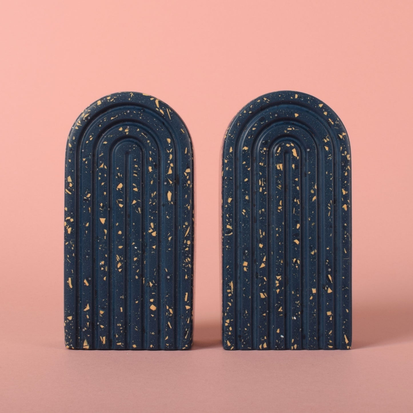 Two small navy blue arched bookends with beige terrazzo chips in them, stood next to each other.