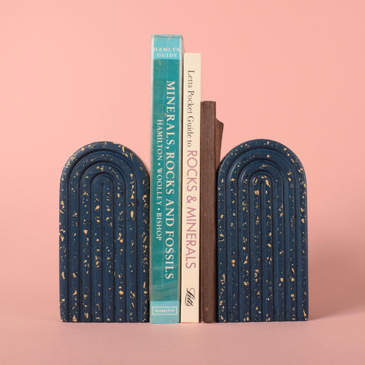 Two small navy blue arched bookends with beige chips in them. Positioned in-between them is 3 books.