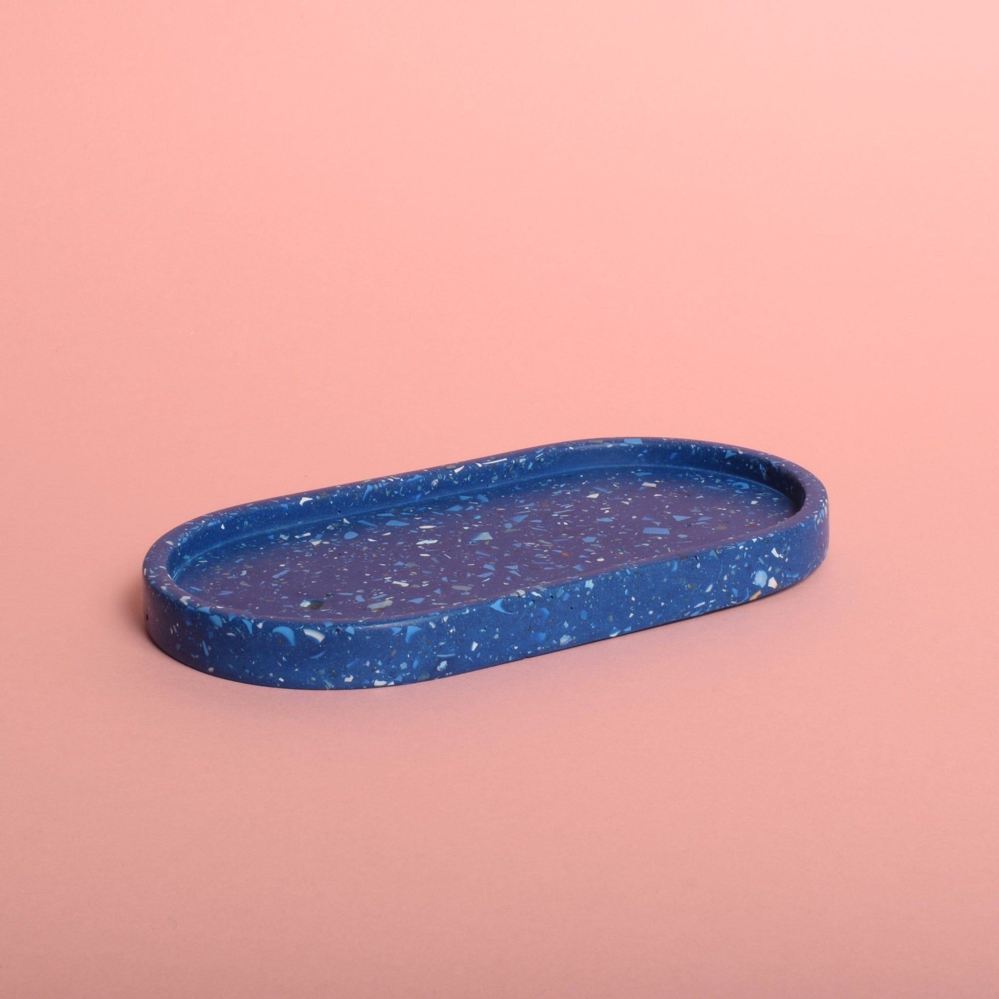 A blue oval trinket tray with blue and white terrazzo chips in it.