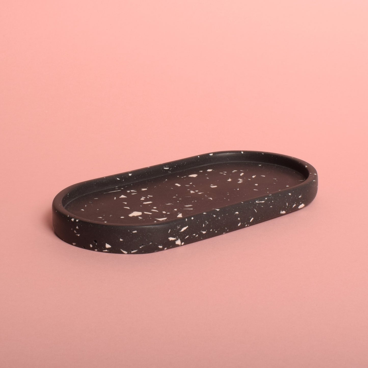 An oval-shaped black trinket tray with white terrazzo chips. 