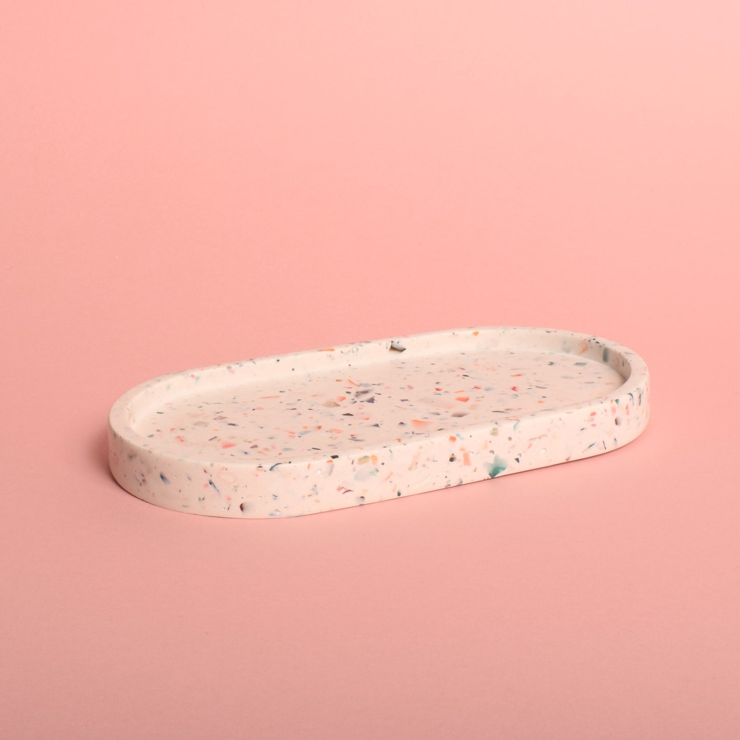 An oval-shaped white trinket tray with multi-coloured terrazzo chips in it.