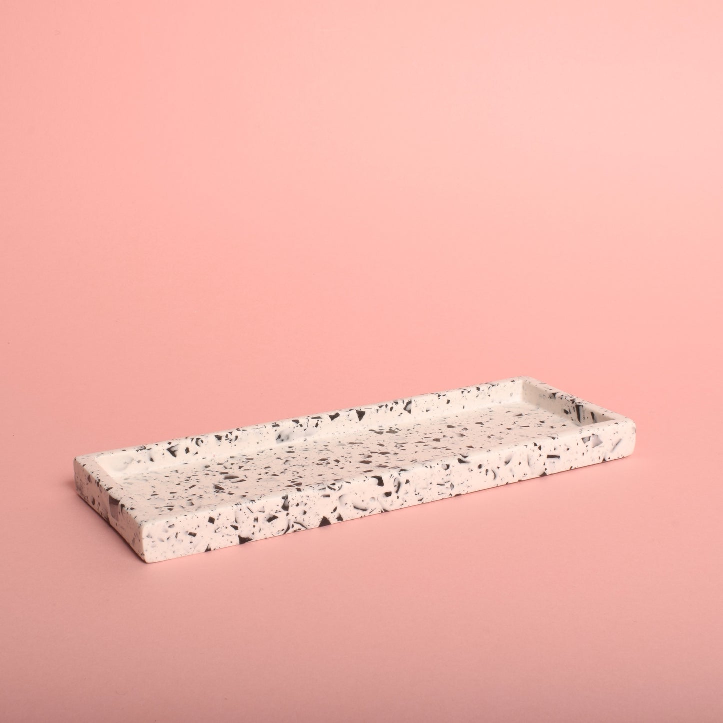 A rectangular white trinket tray with black terrazzo chips in it.