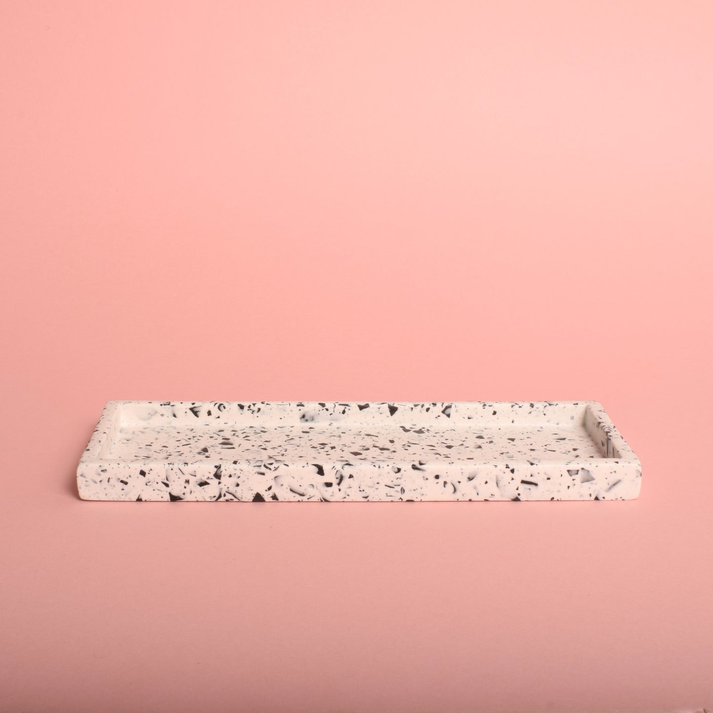 A white rectangular trinket tray with black terrazzo chips in it.