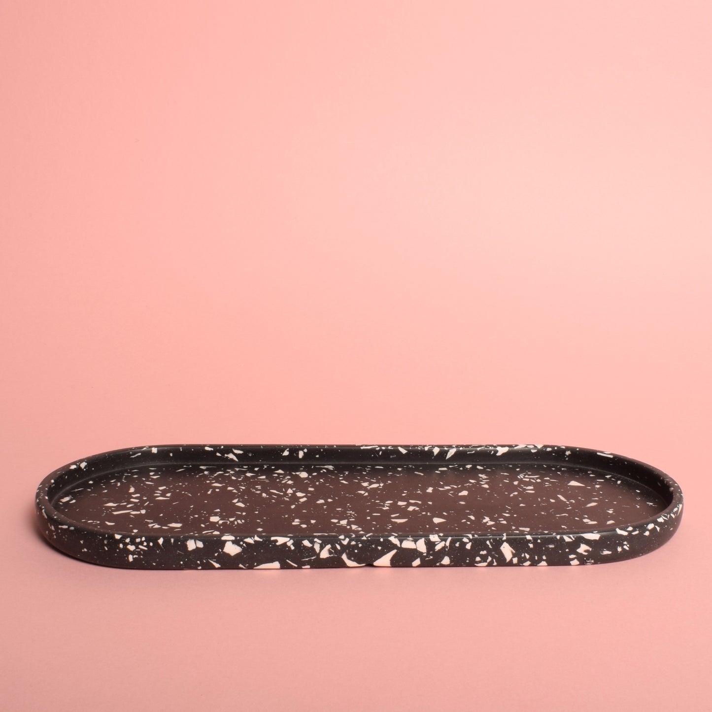 A large oval black trinket tray with white terrazzo chips in it.