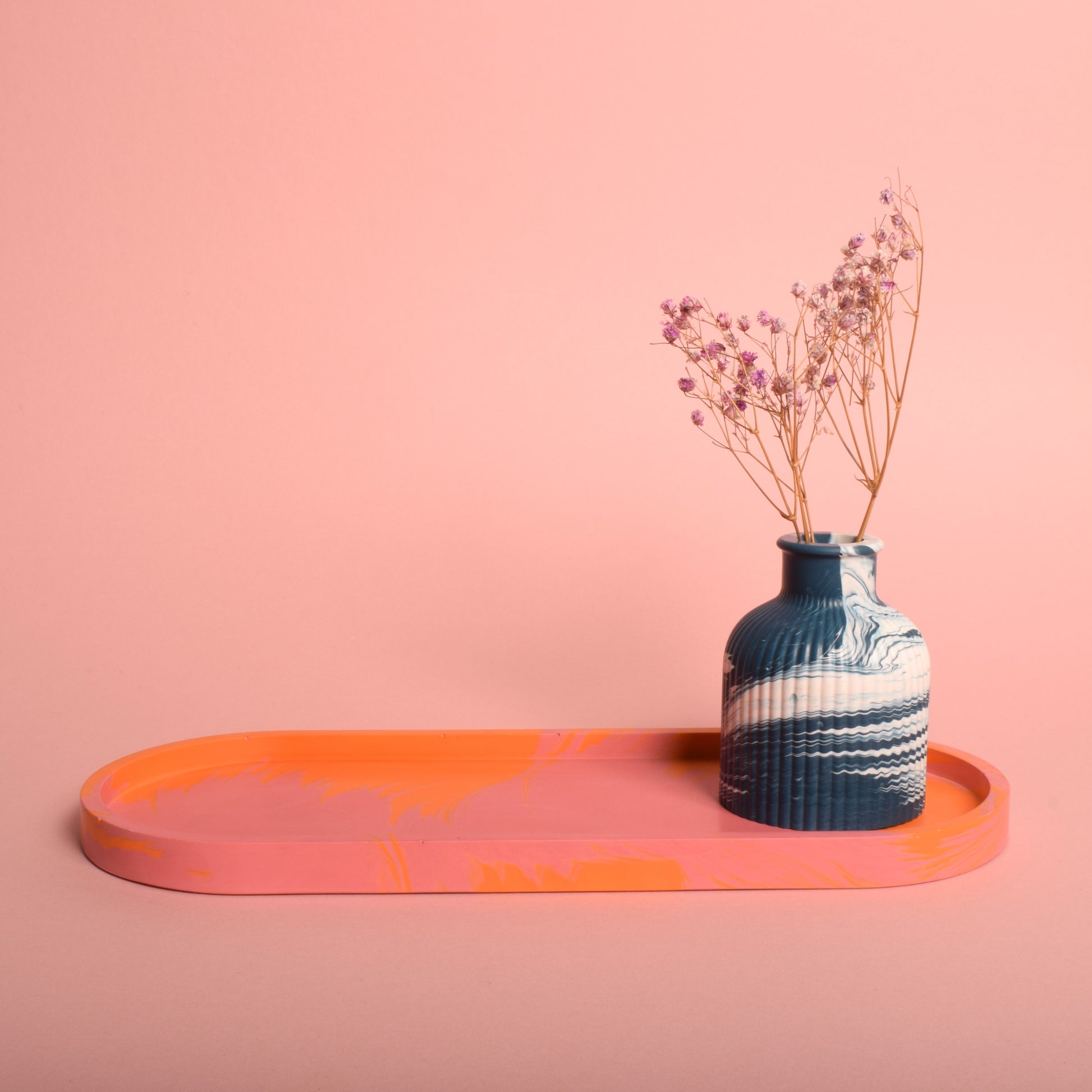 A navy blue and white marble effect ribbed vase holding dried flowers, sitting on a large oval marble effect pink and orange tray.