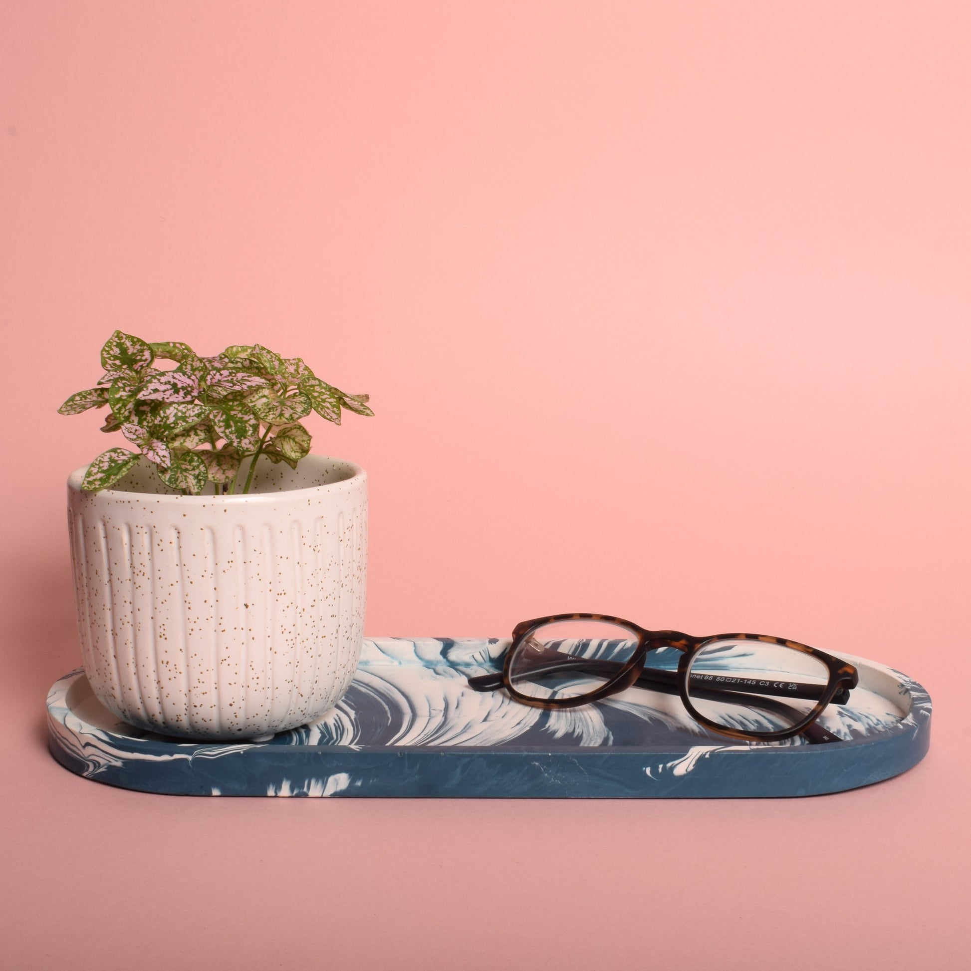 A large oval navy blue and white marble effect trinket tray, holding a pair of glasses and a plant pot.