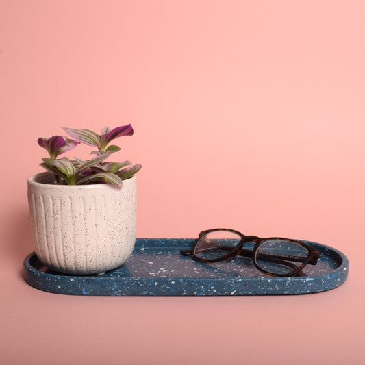 A large oval blue terrazzo trinket tray, holding a pair of glasses and a plant pot.