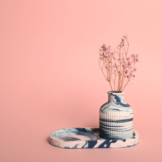 A navy blue and white marble effect oval trinket tray. The tray is holding a blue and white marble effect vase, which is holding dried flowers