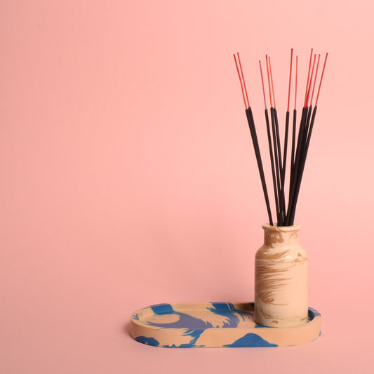 A blue and beige marble effect oval trinket tray holding a beige marble effect vase, which is holding incense sticks