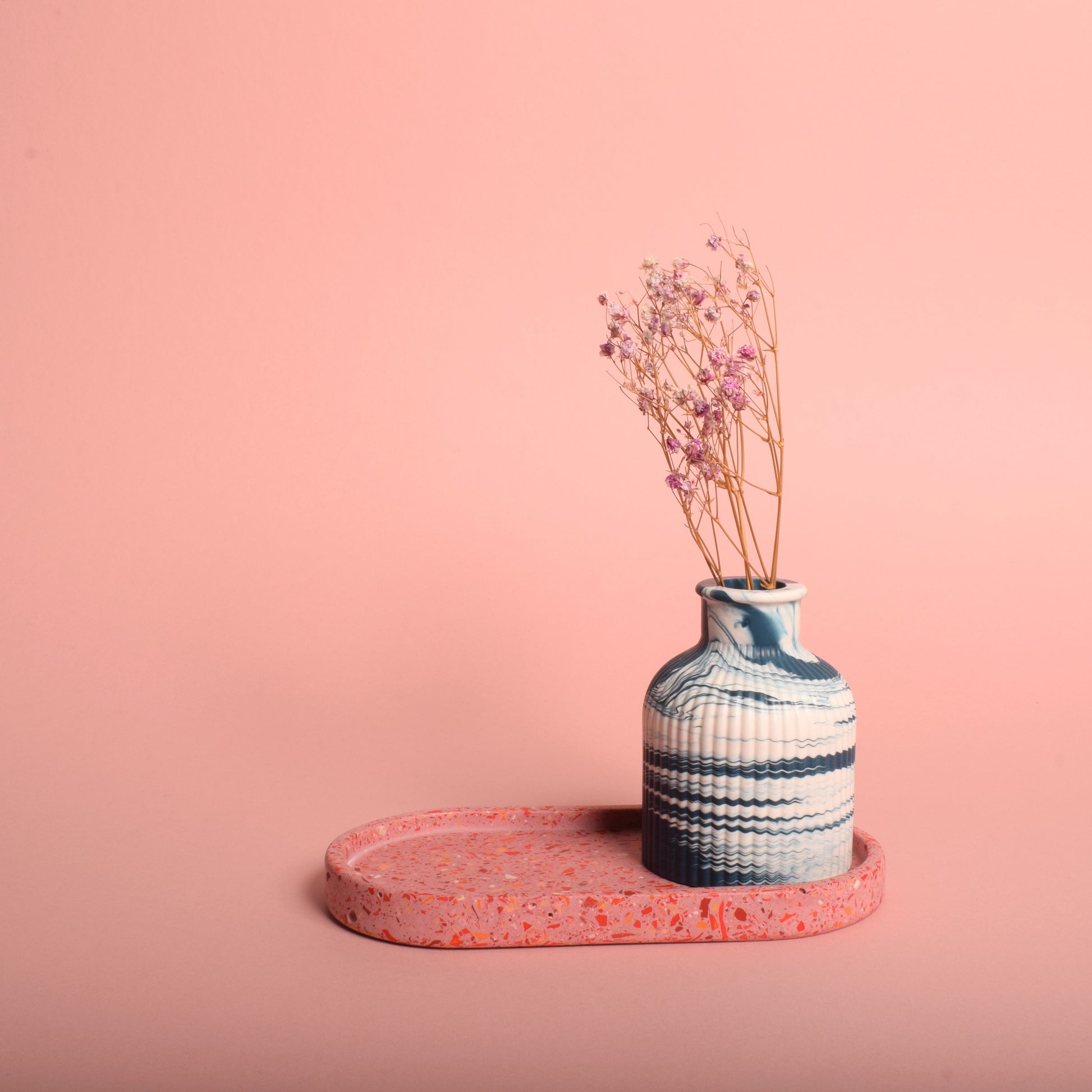 A navy blue and white marble effect ribbed vase holding dried flowers, sitting on a pink oval terrazzo tray.