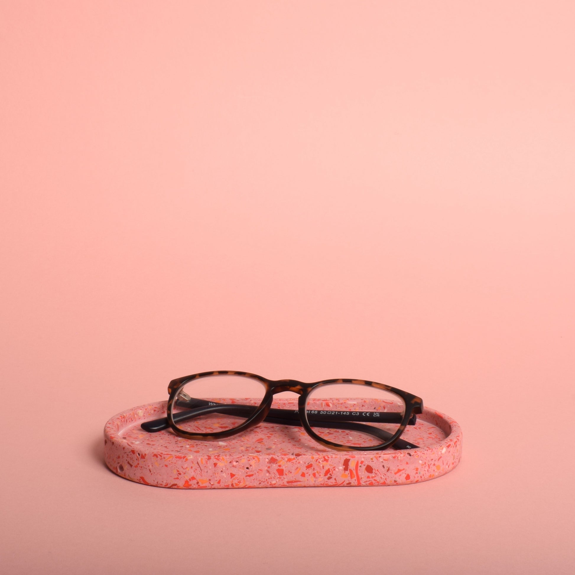 An oval pink terrazzo trinket tray holding a pair of glasses